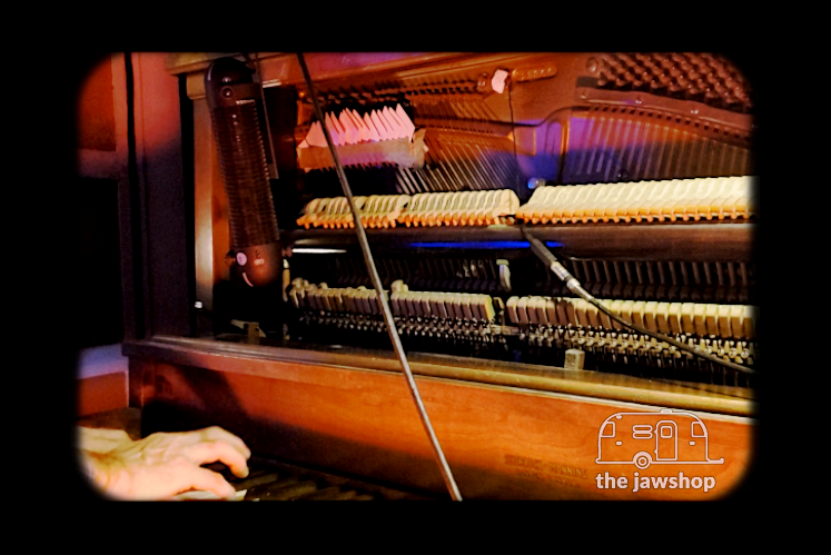 Still image of a microphone attached to a piano from the Prepared Piano video by the Jawshop Adventure Recording Studios.